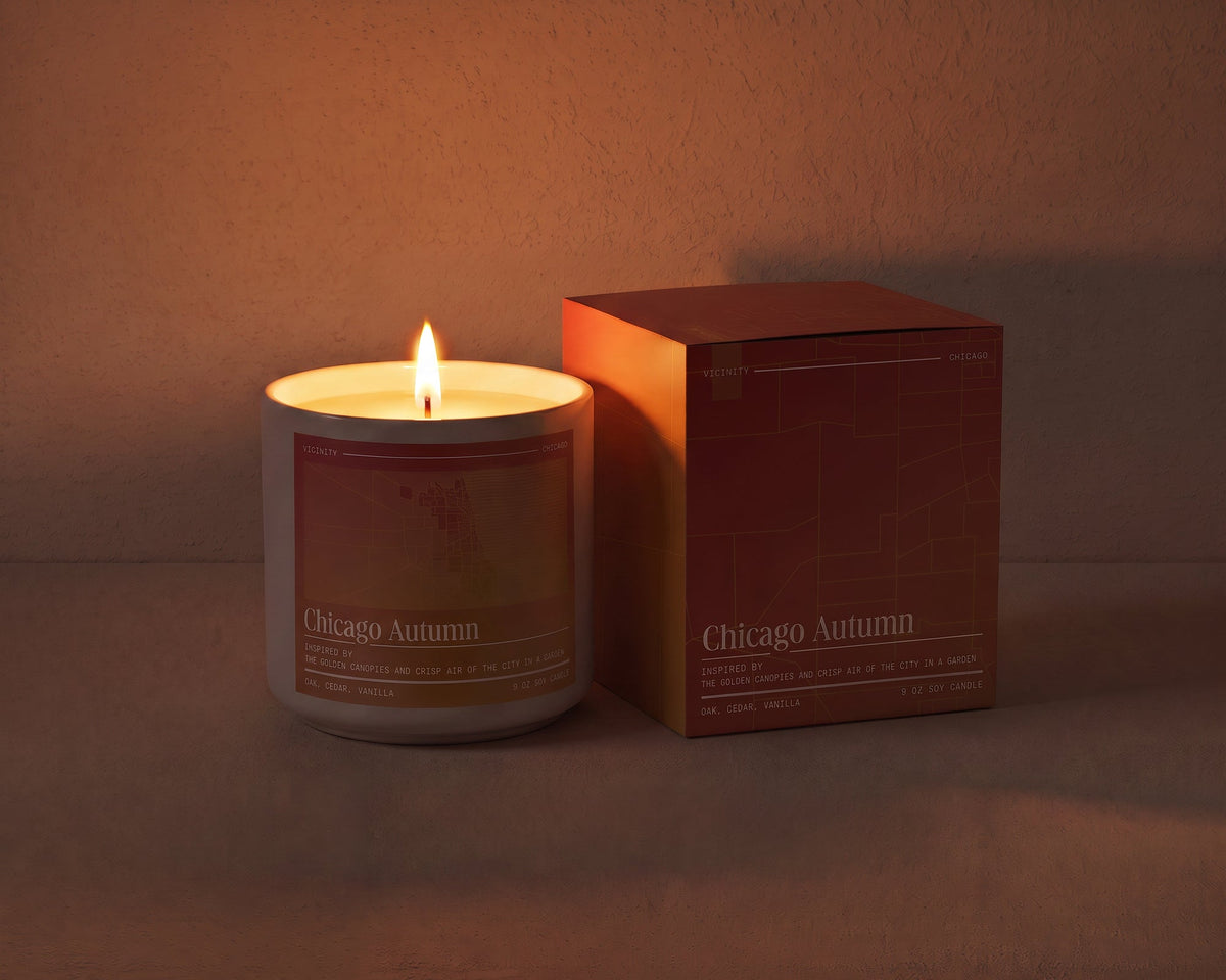 Chicago Autumn 9 oz soy candle lit beside its gift box, the room lit only by the candle flame