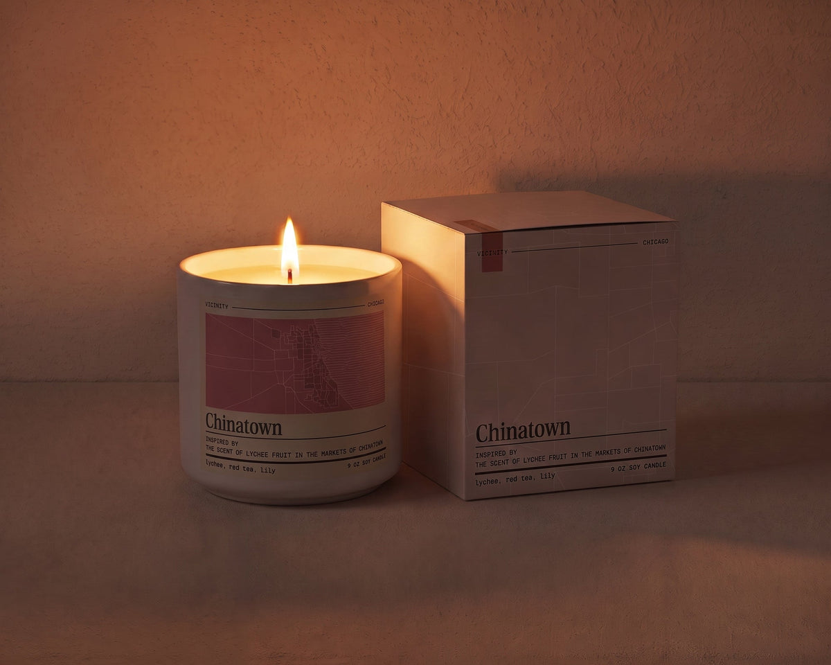 Chinatown 9 oz soy candle lit beside its gift box, the room lit only by the candle flame