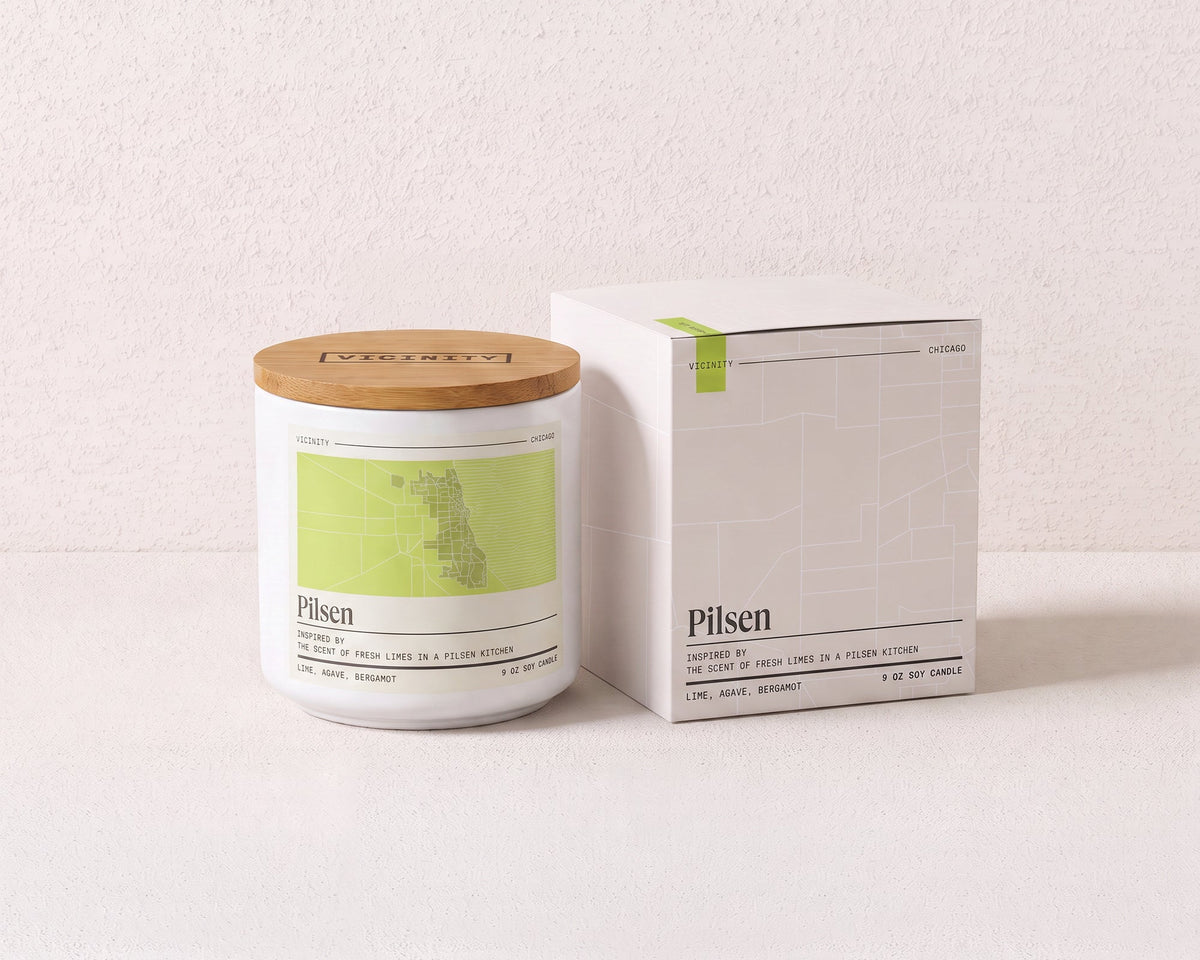 Pilsen 9 oz soy candle and its gift box, both printed with a Chicago neighborhood map, on a cream plaster surface