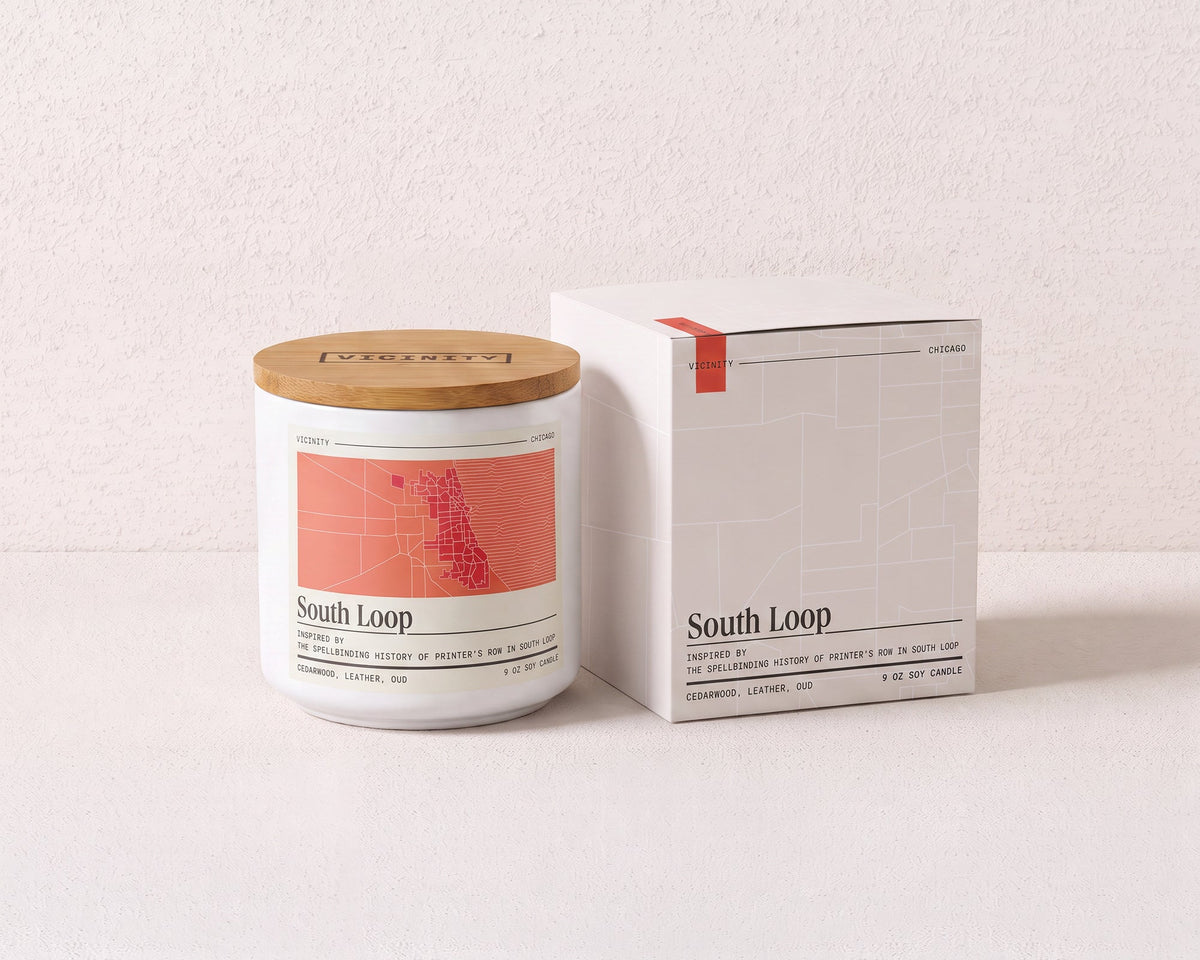 South Loop 9 oz soy candle and its gift box, both printed with a Chicago neighborhood map, on a cream plaster surface