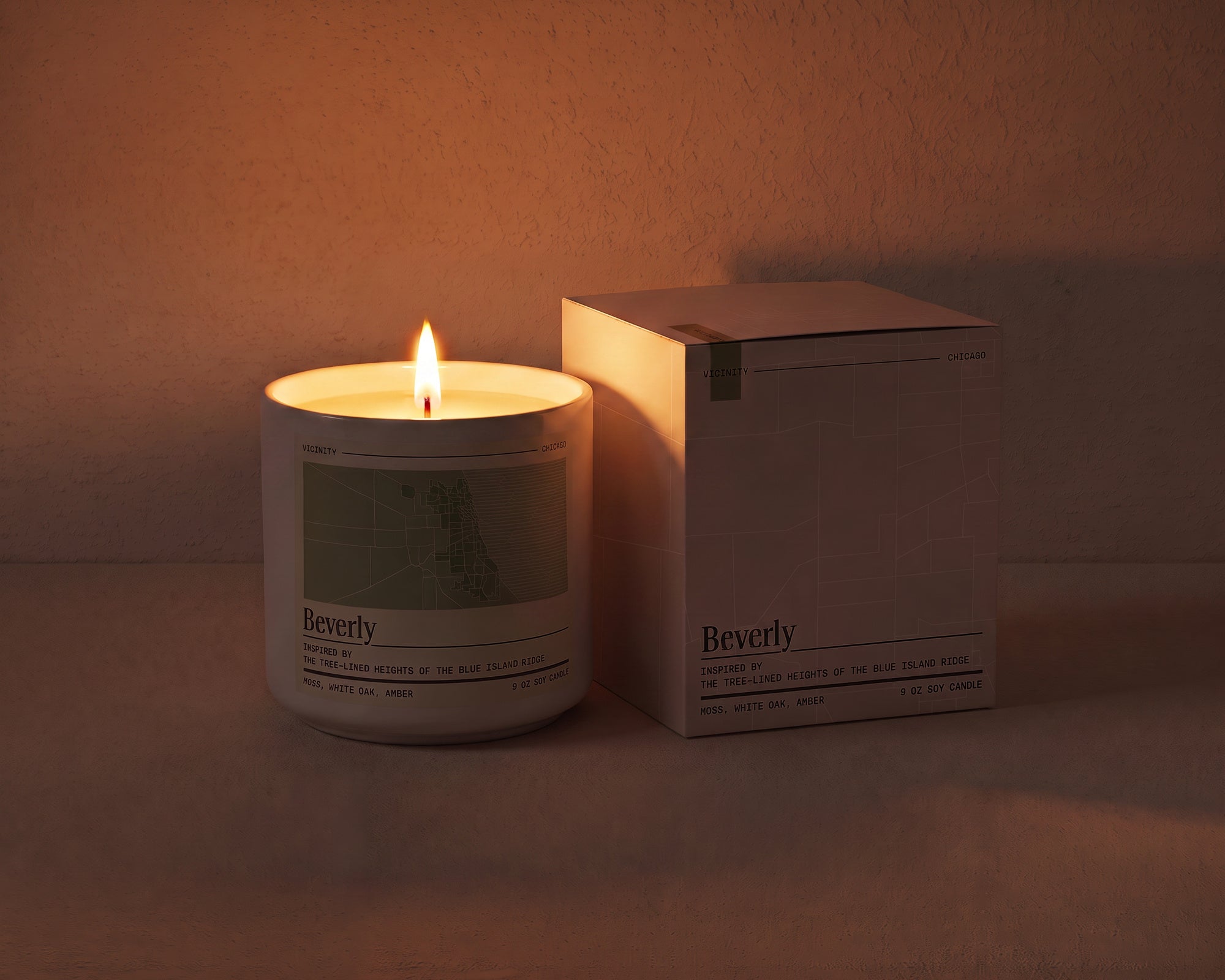 Beverly 9 oz soy candle lit beside its gift box, the room lit only by the candle flame