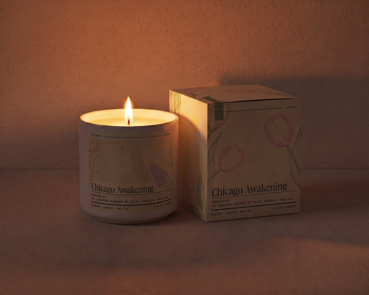 Chicago Awakening 9 oz soy candle lit beside its gift box, the room lit only by the candle flame