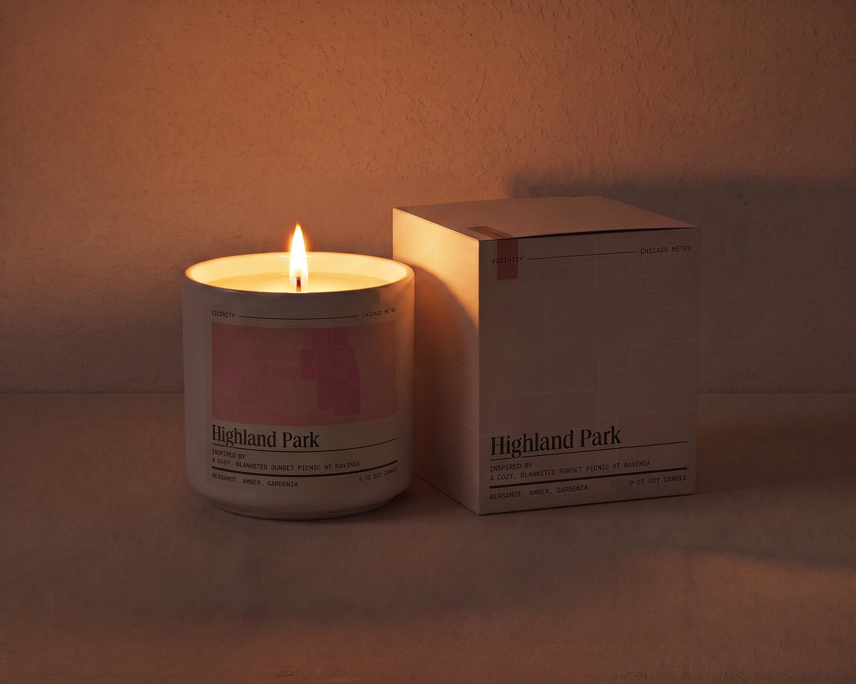 Highland Park 9 oz soy candle lit beside its gift box, the room lit only by the candle flame