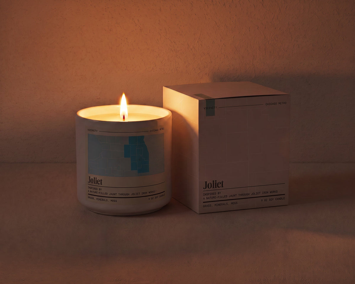 Joliet 9 oz soy candle lit beside its gift box, the room lit only by the candle flame