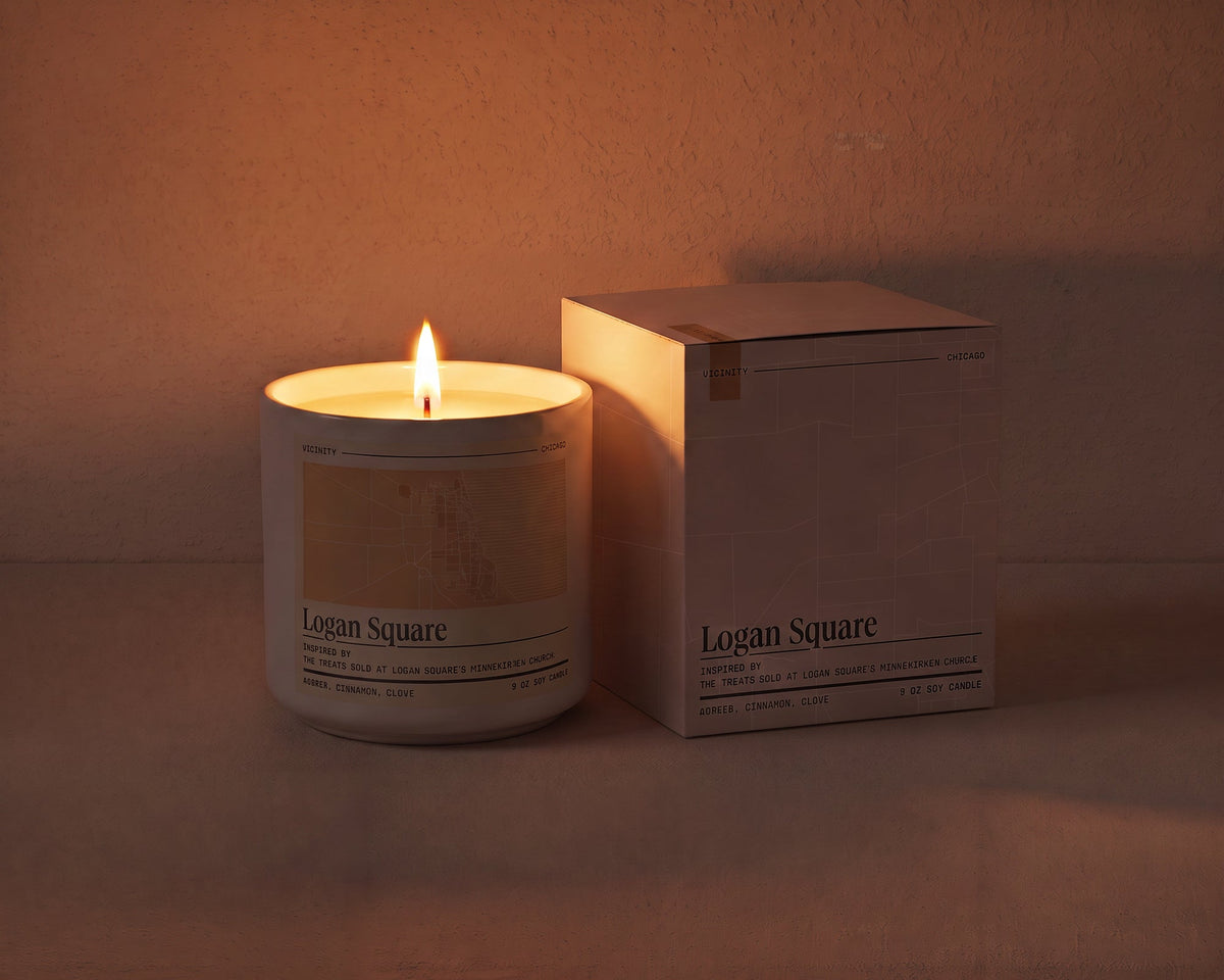 Logan Square 9 oz soy candle lit beside its gift box, the room lit only by the candle flame
