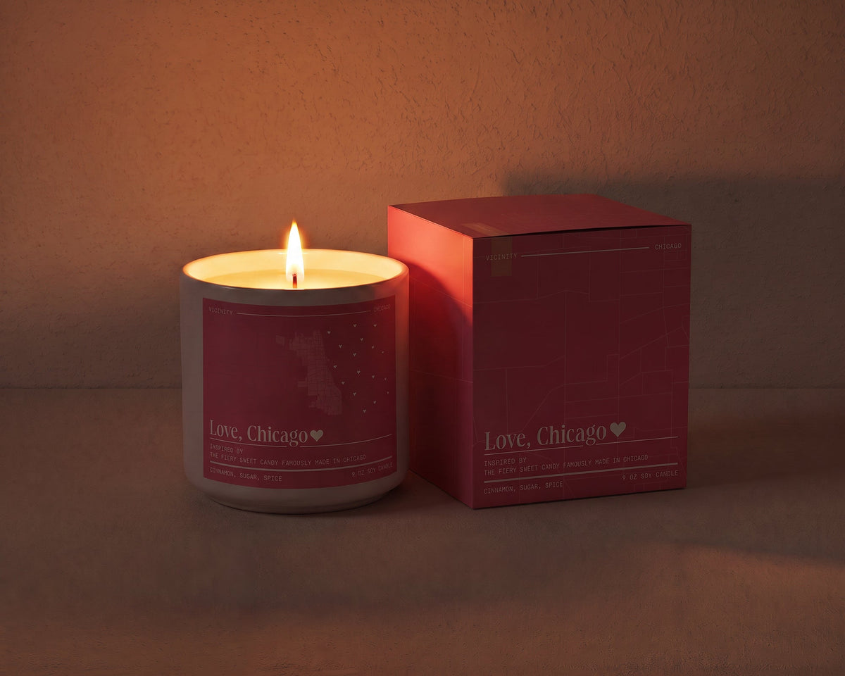 Love, Chicago 9 oz soy candle lit beside its gift box, the room lit only by the candle flame