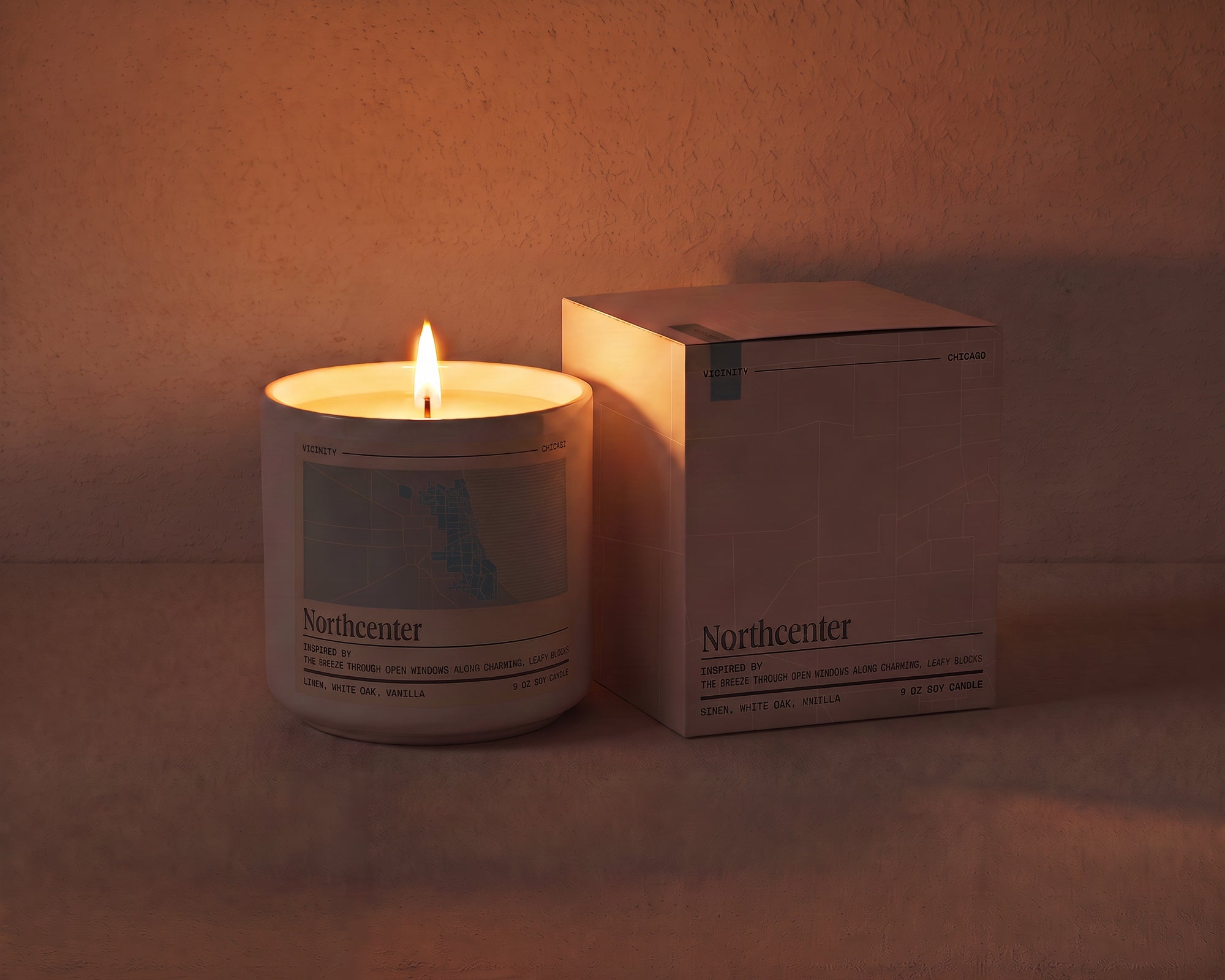 Northcenter 9 oz soy candle lit beside its gift box, the room lit only by the candle flame
