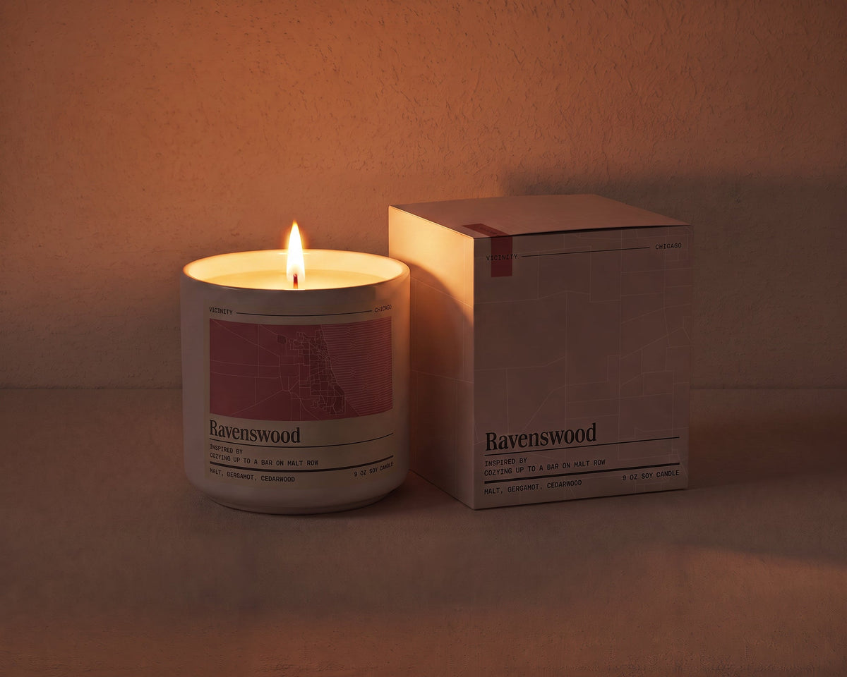 Ravenswood 9 oz soy candle lit beside its gift box, the room lit only by the candle flame