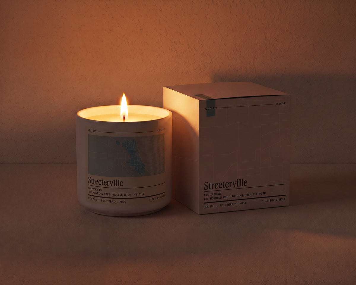 Streeterville 9 oz soy candle lit beside its gift box, the room lit only by the candle flame