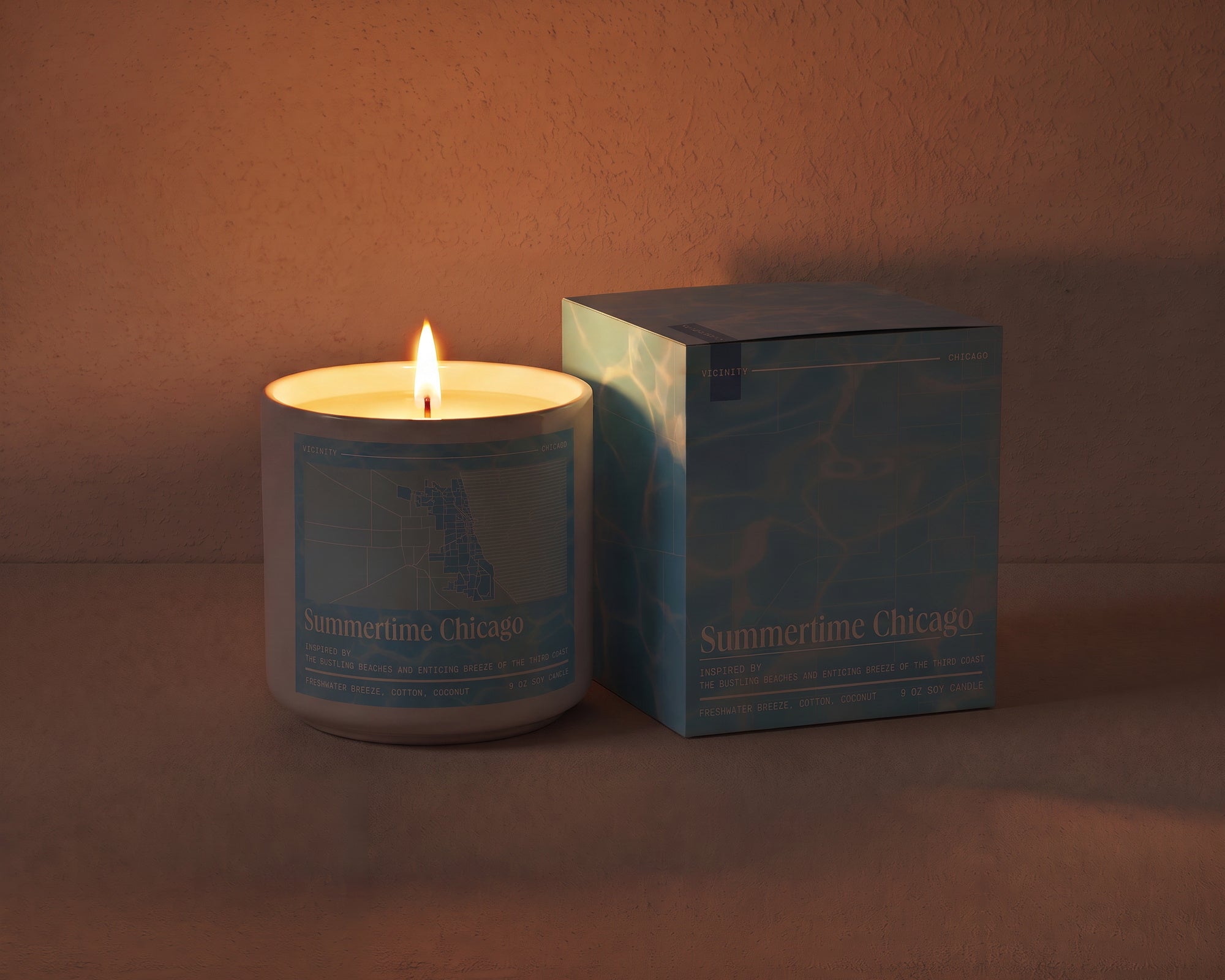 Summertime Chicago 9 oz soy candle and its gift box, both printed with a Chicago neighborhood map, on a cream plaster surface