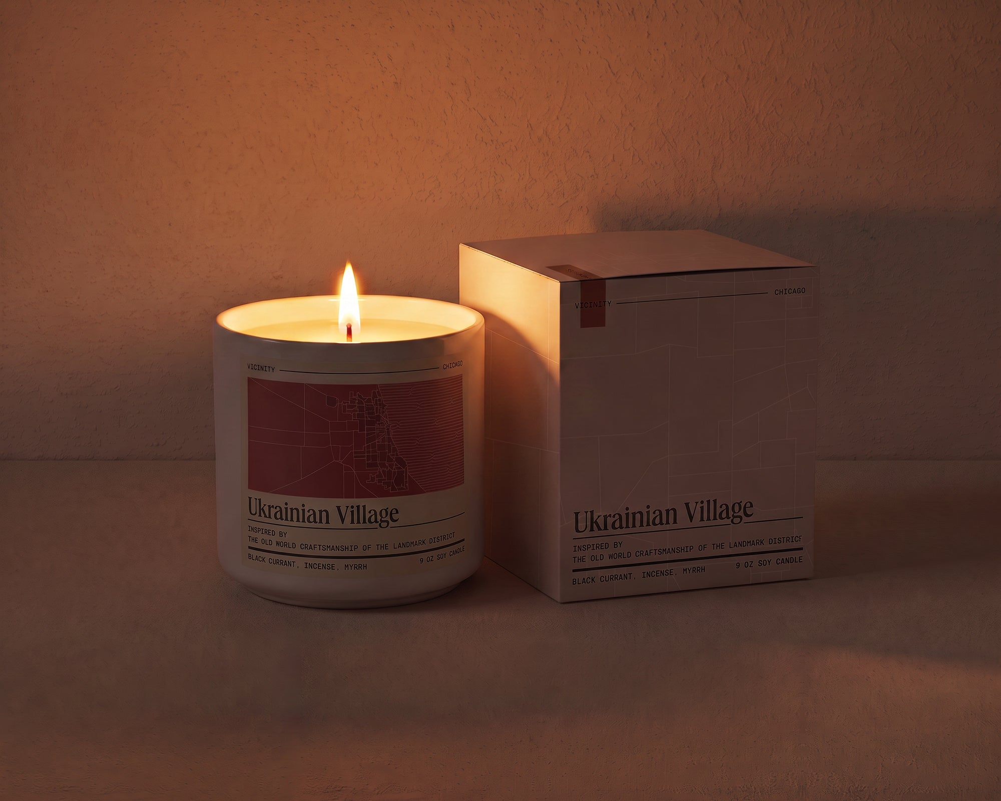Ukrainian Village 9 oz soy candle lit beside its gift box, the room lit only by the candle flame