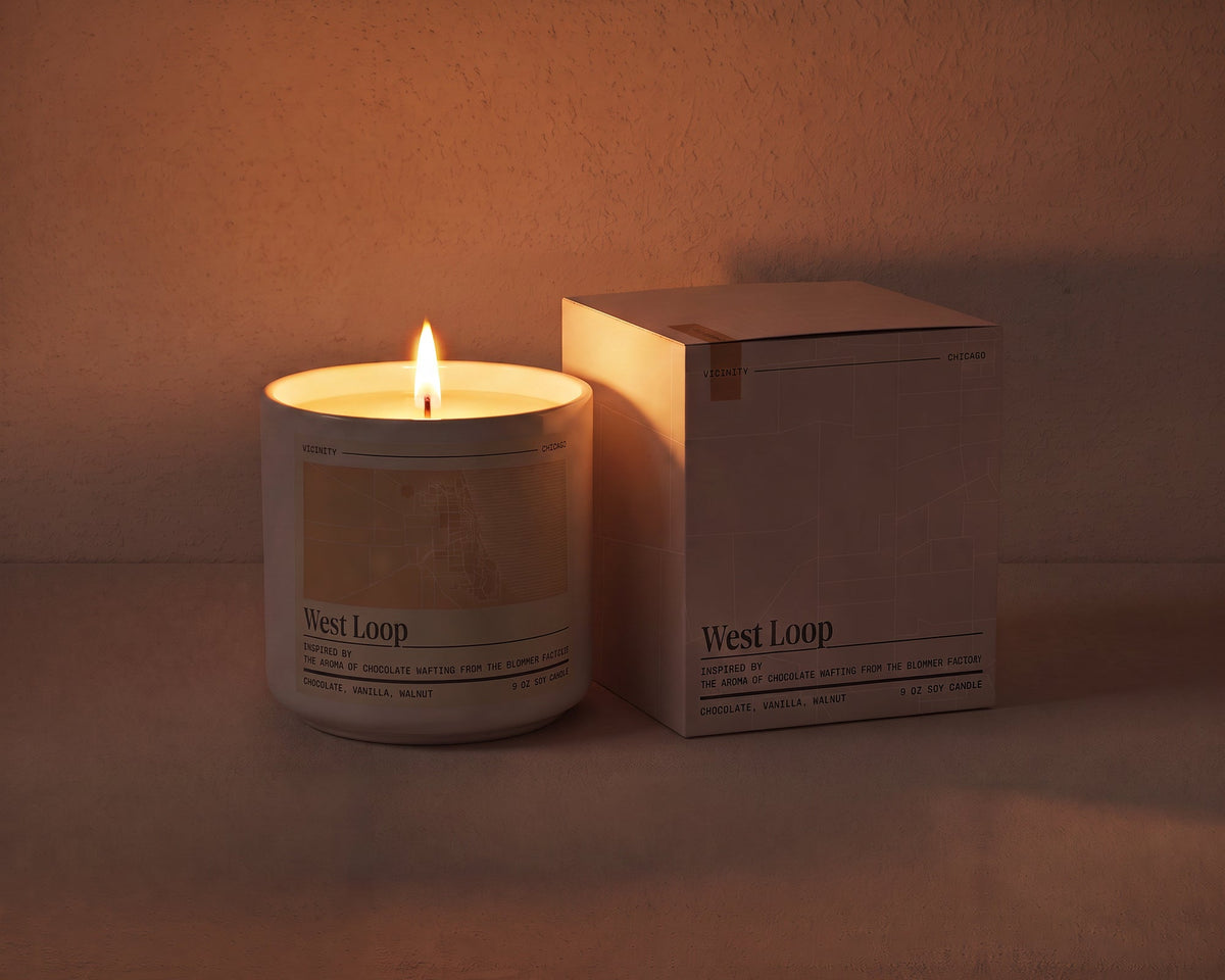 West Loop 9 oz soy candle lit beside its gift box, the room lit only by the candle flame