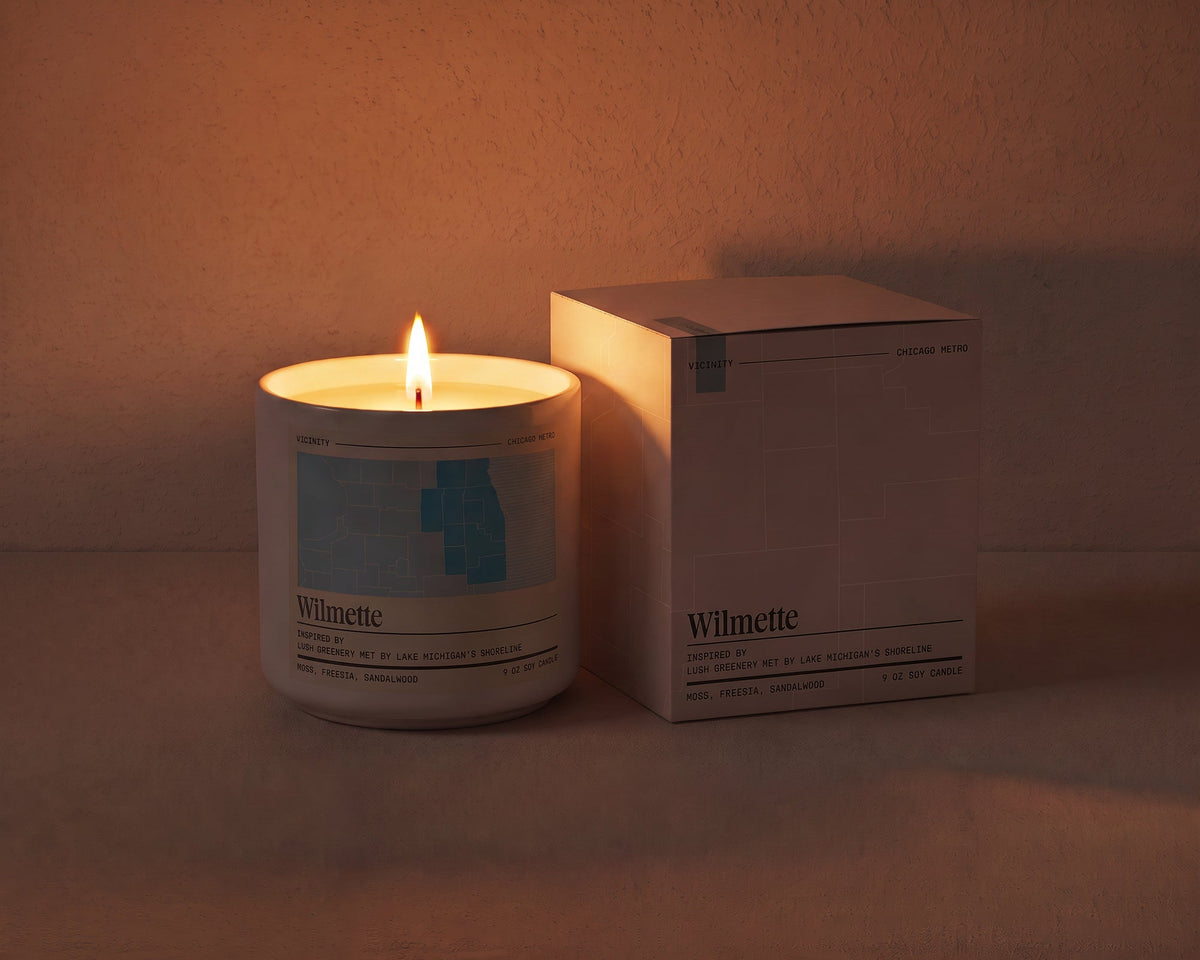 Wilmette 9 oz soy candle lit beside its gift box, the room lit only by the candle flame