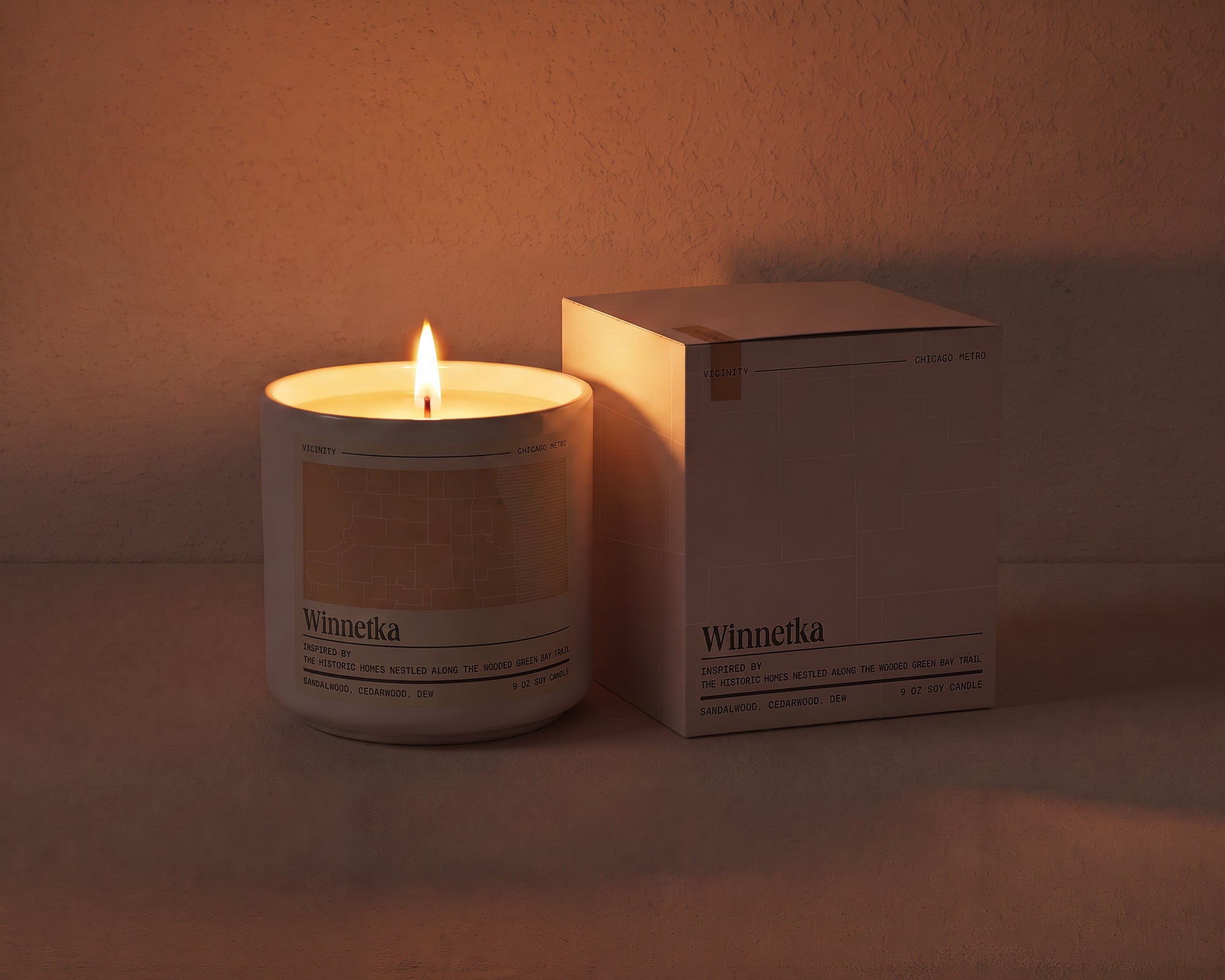 Winnetka 9 oz soy candle lit beside its gift box, the room lit only by the candle flame