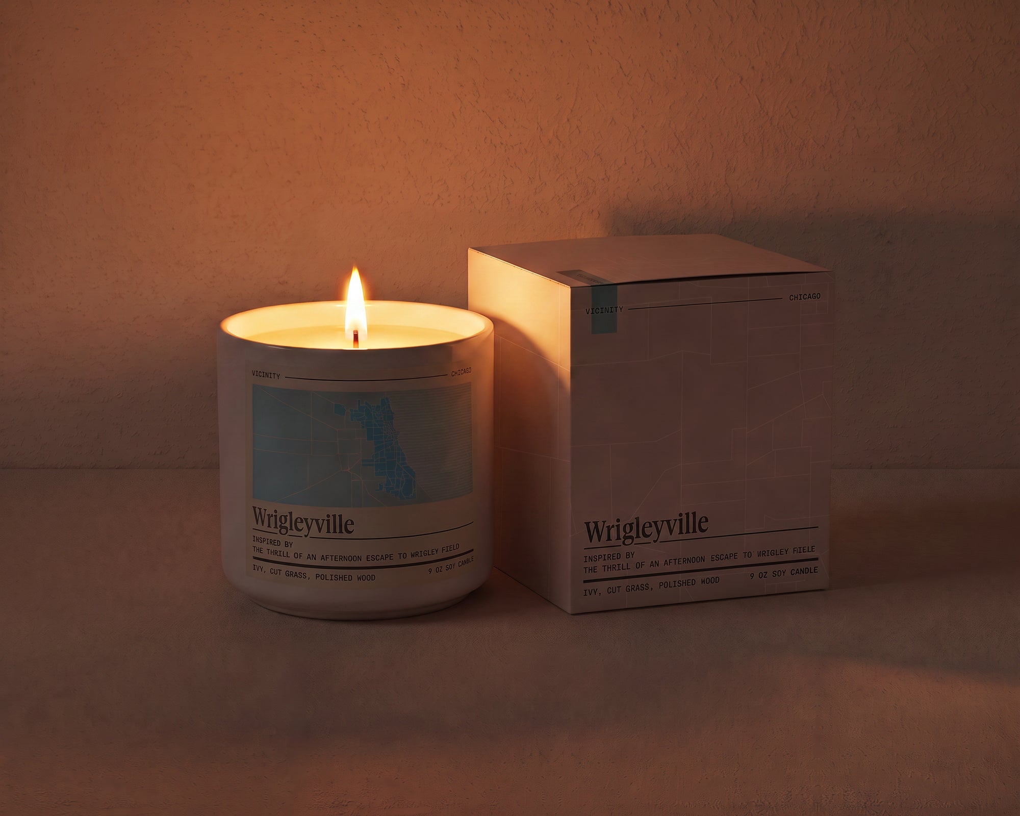 Wrigleyville 9 oz soy candle and its gift box, both printed with a Chicago neighborhood map, on a cream plaster surface