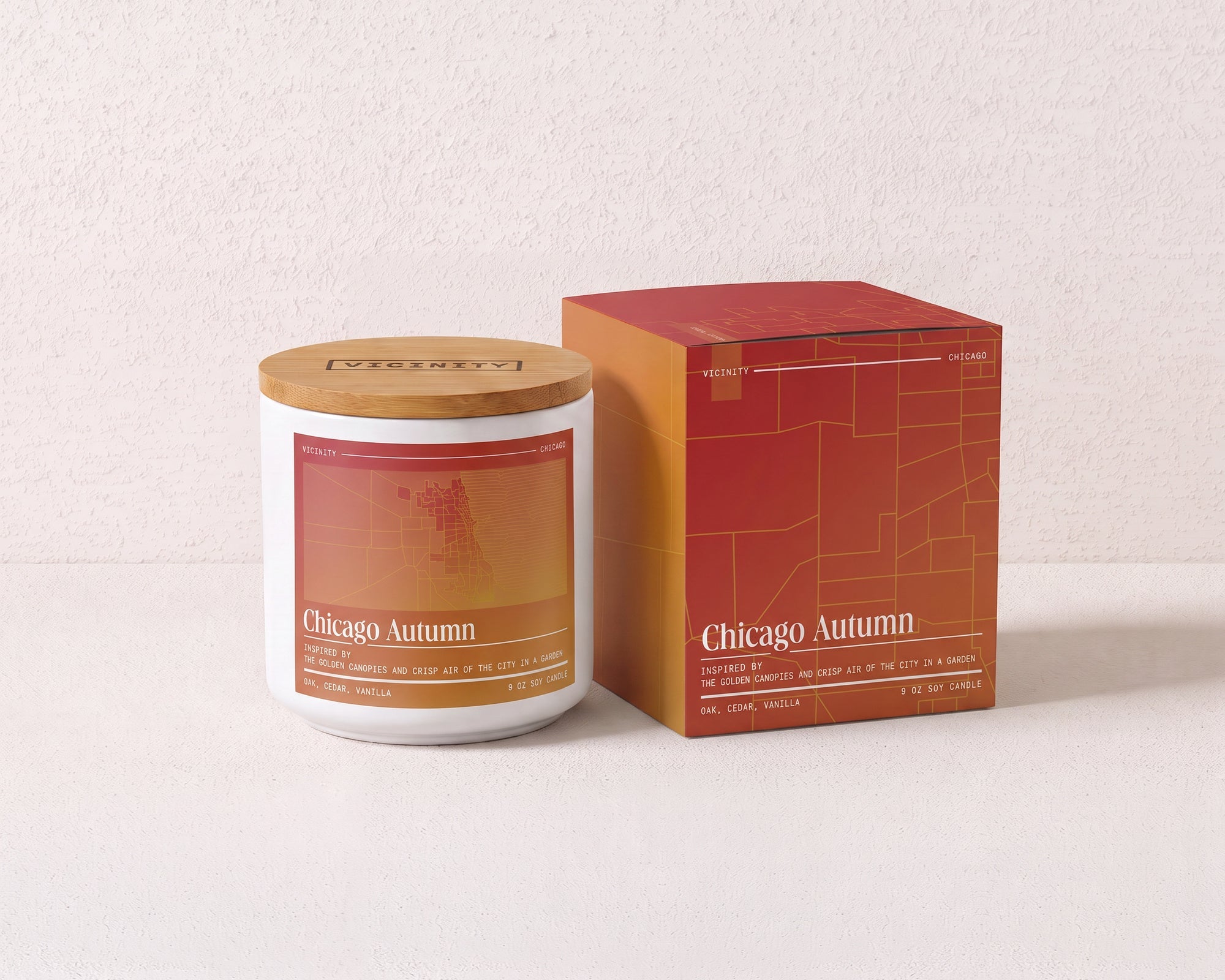 Chicago Autumn 9 oz soy candle and its gift box, both printed with a Chicago neighborhood map, on a cream plaster surface