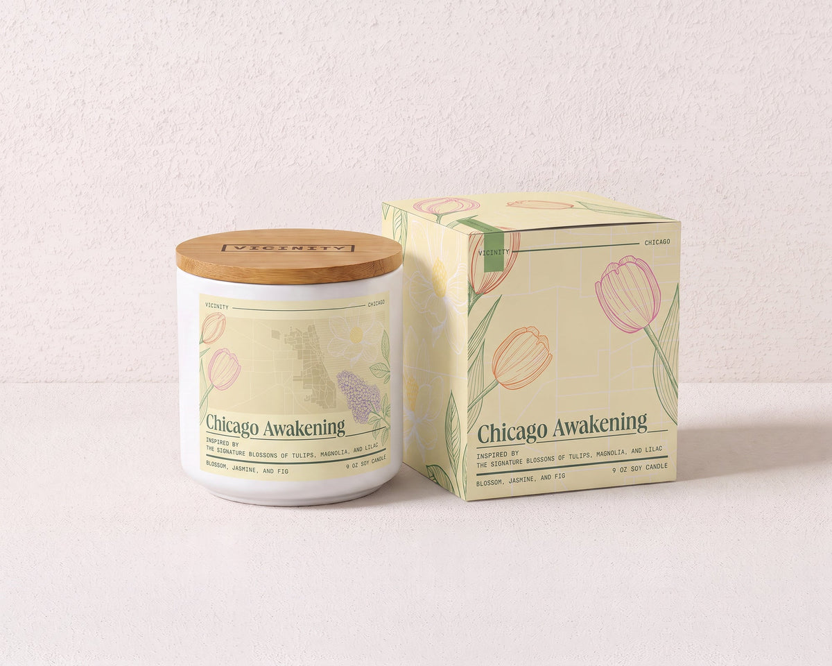 Chicago Awakening 9 oz soy candle and its gift box, both printed with a Chicago neighborhood map, on a cream plaster surface