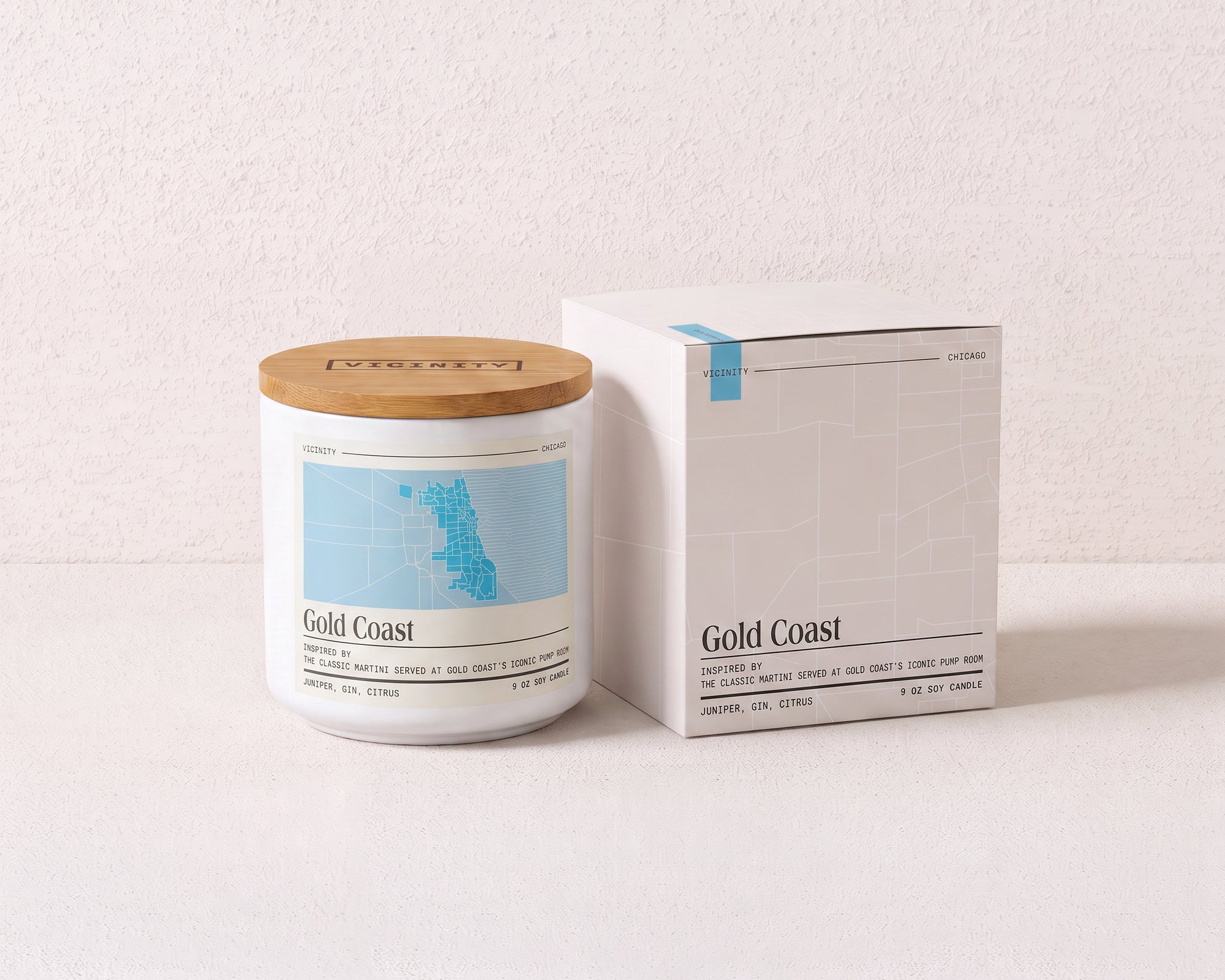 Gold Coast 9 oz soy candle and its gift box, both printed with a Chicago neighborhood map, on a cream plaster surface