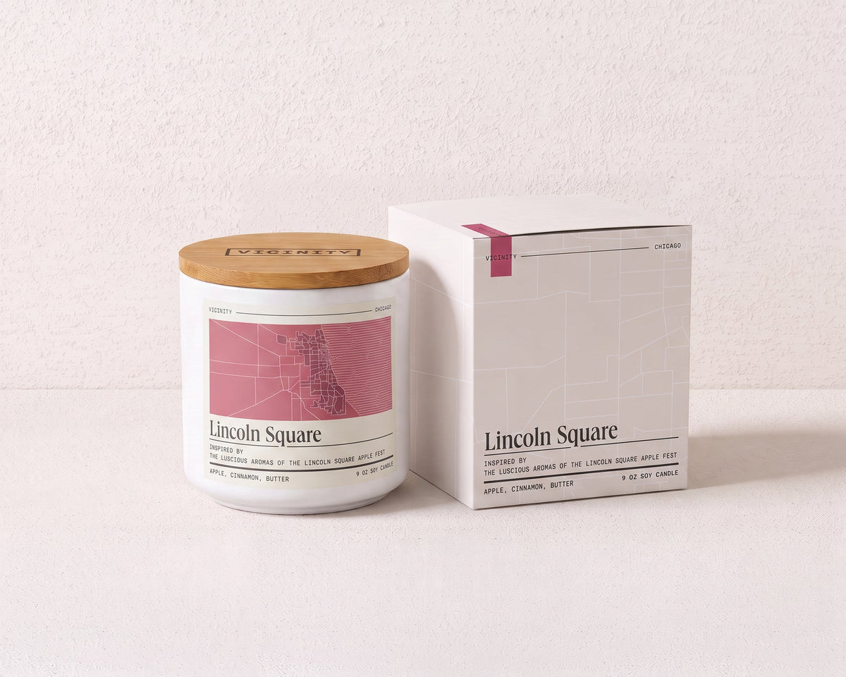 Lincoln Square 9 oz soy candle and its gift box, both printed with a Chicago neighborhood map, on a cream plaster surface