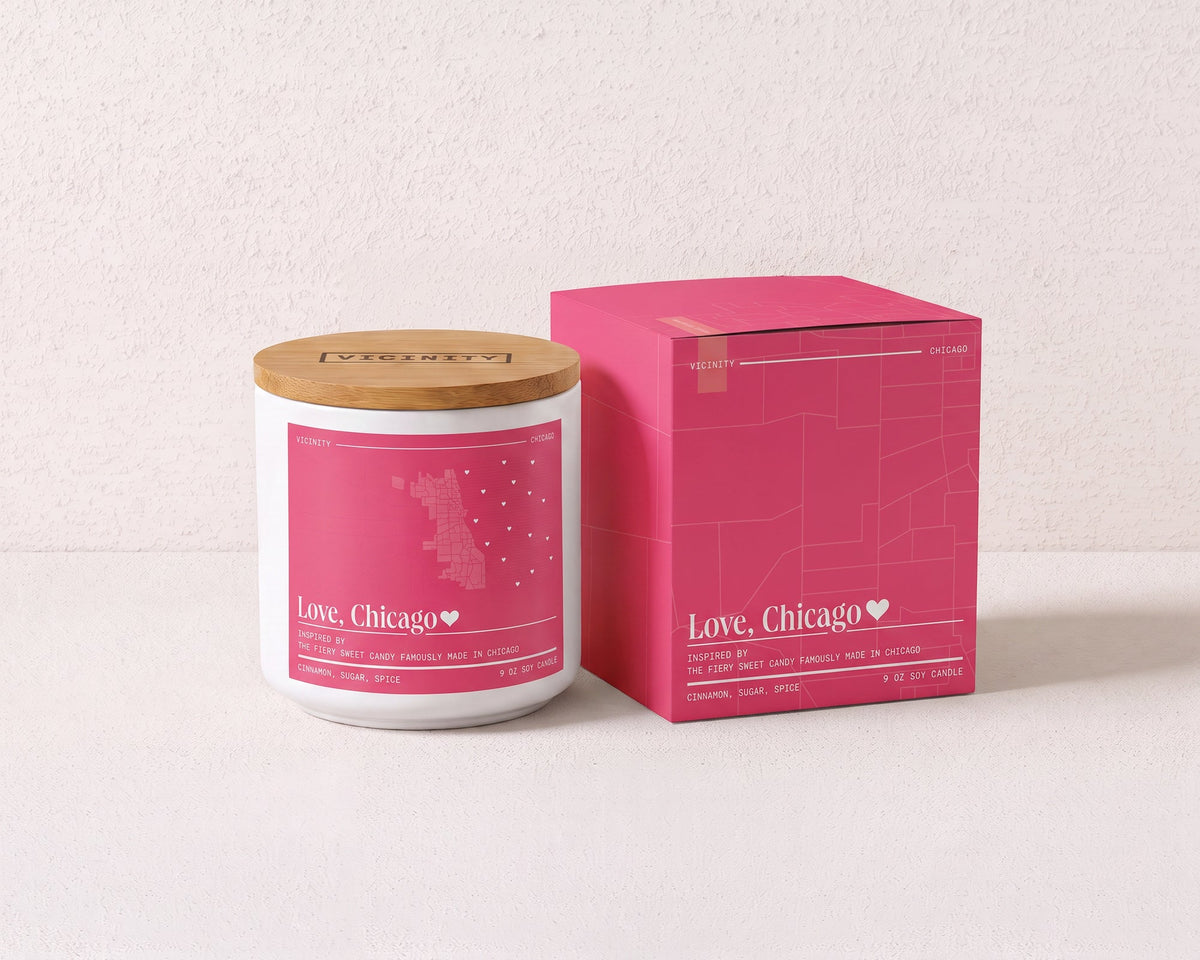 Love, Chicago 9 oz soy candle and its gift box, both printed with a Chicago neighborhood map, on a cream plaster surface