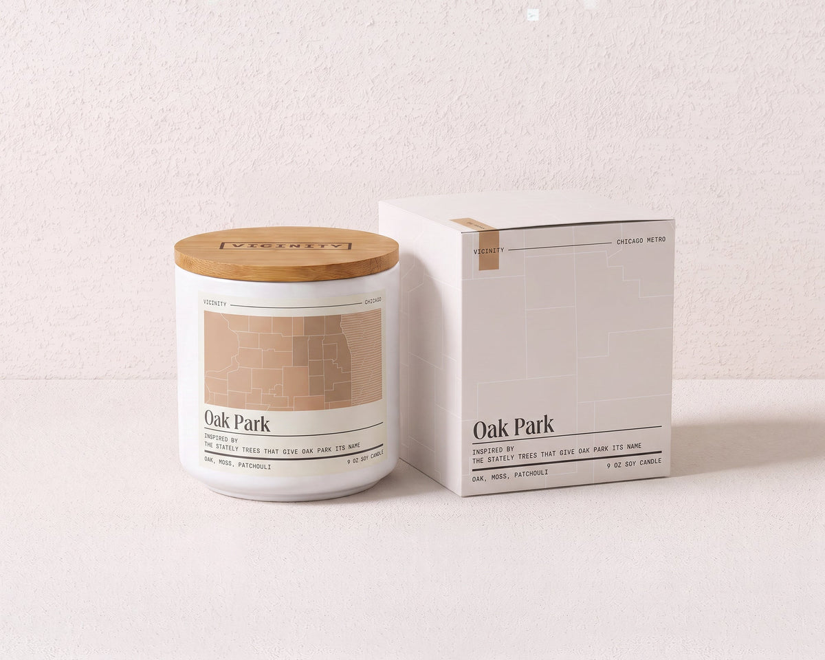 Oak Park 9 oz soy candle and its gift box, both printed with a Chicago neighborhood map, on a cream plaster surface