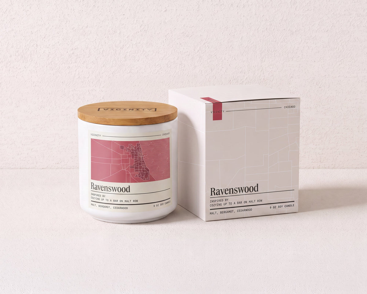 Ravenswood 9 oz soy candle and its gift box, both printed with a Chicago neighborhood map, on a cream plaster surface