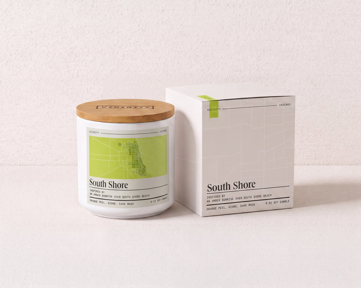 South Shore 9 oz soy candle and its gift box, both printed with a Chicago neighborhood map, on a cream plaster surface
