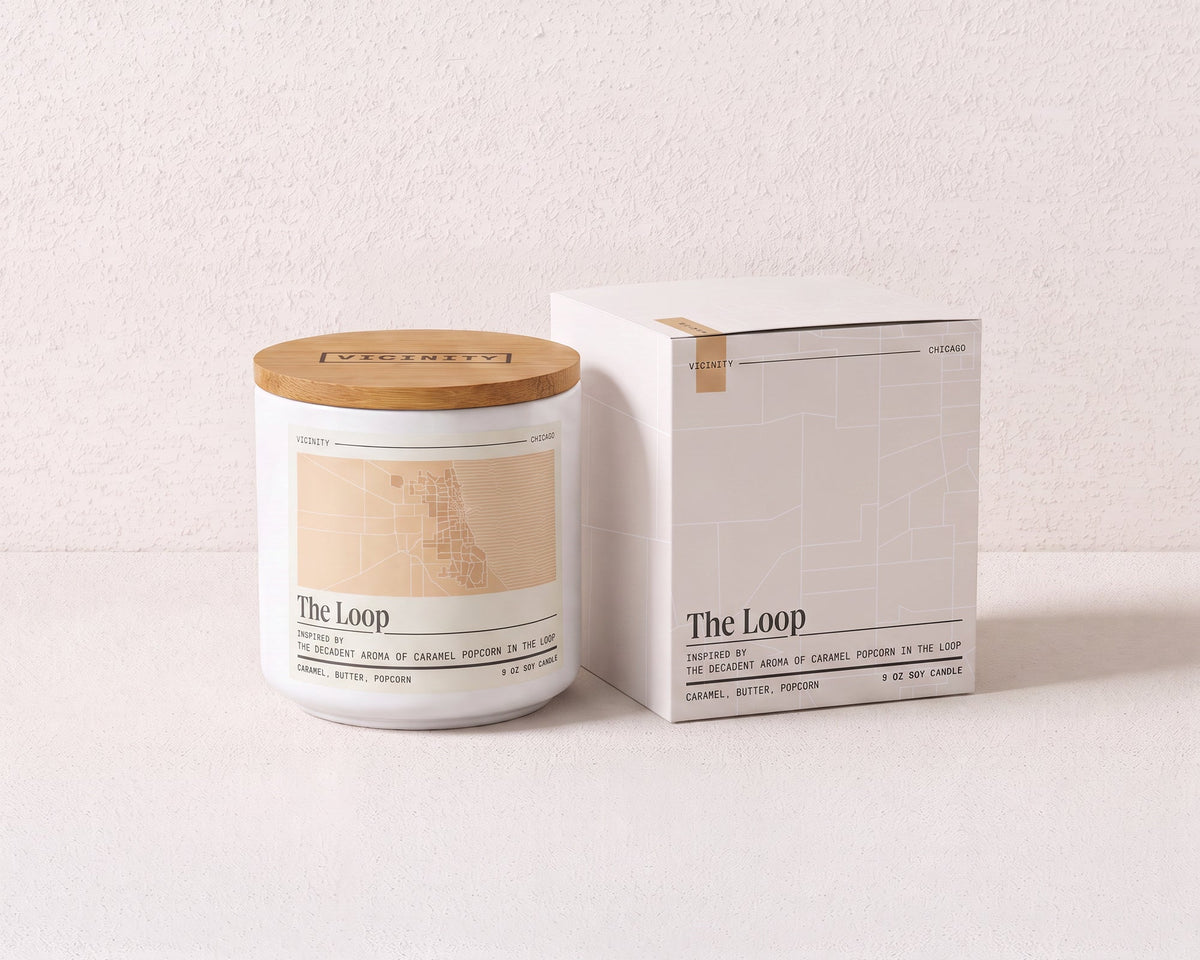 The Loop 9 oz soy candle and its gift box, both printed with a Chicago neighborhood map, on a cream plaster surface