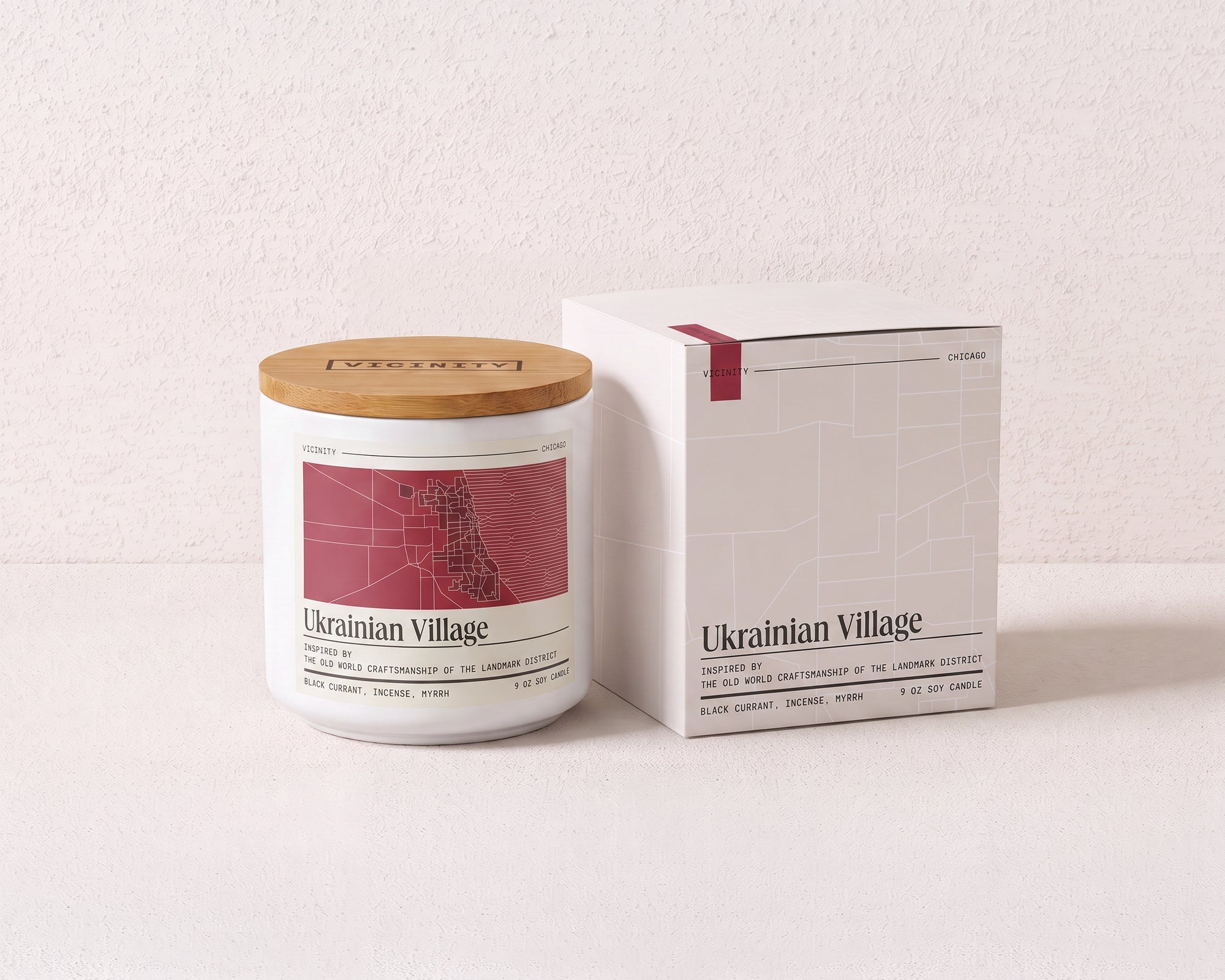 Ukrainian Village 9 oz soy candle and its gift box, both printed with a Chicago neighborhood map, on a cream plaster surface