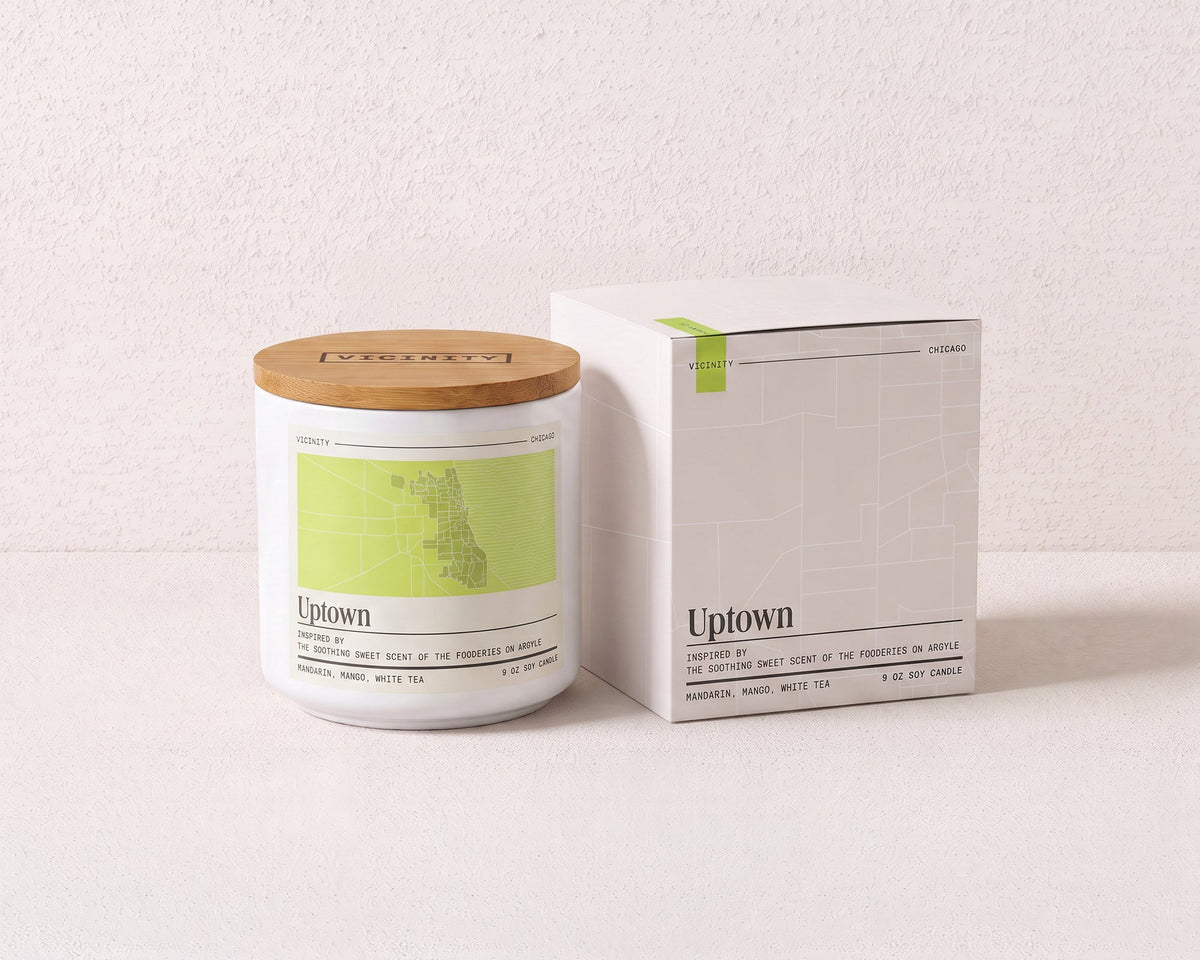 Uptown 9 oz soy candle and its gift box, both printed with a Chicago neighborhood map, on a cream plaster surface