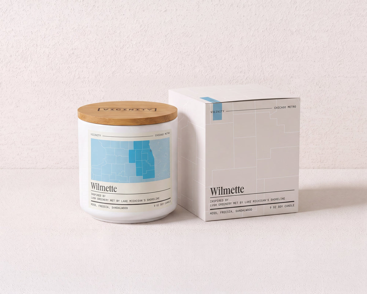 Wilmette 9 oz soy candle and its gift box, both printed with a Chicago neighborhood map, on a cream plaster surface